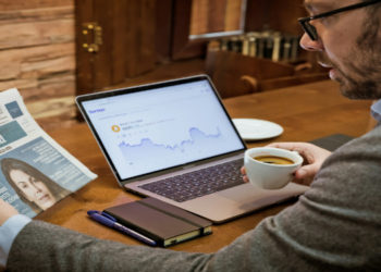 Investment chart on a laptop screen and a man holding a newspaper about the economy
