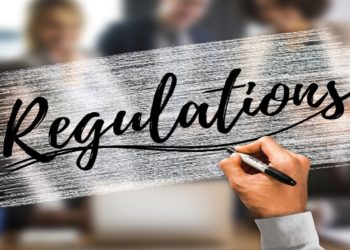 hand writing the word Regulations to a clear board