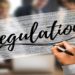 hand writing the word Regulations to a clear board