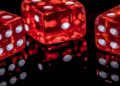 Three red casino dice displayed closely against a black background, showcasing their pips and vibrant color.