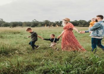 Cheerful family walks hand in hand through a lush field, embracing a moment of togetherness in nature.