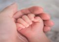 Person gently holds a baby's hand, symbolizing connection and care between them.