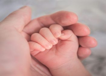 Person gently holds a baby's hand, symbolizing connection and care between them.