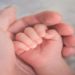 Person gently holds a baby's hand, symbolizing connection and care between them.