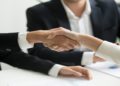 Two professionals shaking hands over a conference table, symbolizing agreement and collaboration.