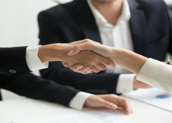Two professionals shaking hands over a conference table, symbolizing agreement and collaboration.