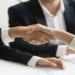 Two professionals shaking hands over a conference table, symbolizing agreement and collaboration.