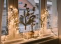 Cozy window decorated with string lights and glass vases holding cotton branches. Soft light creates a warm, festive ambiance.