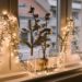 Cozy window decorated with string lights and glass vases holding cotton branches. Soft light creates a warm, festive ambiance.