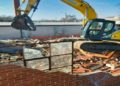 Yellow excavator demolishes a brick wall at a house under demolition