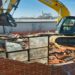 Yellow excavator demolishes a brick wall at a house under demolition