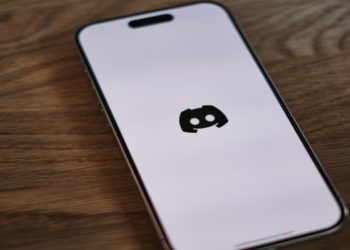 Smartphone on a wooden table displays the Discord logo on its screen. The tone is neutral and tech-focused, highlighting modern digital communication.