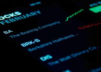 Close-up of a smartphone screen showing stock data with a dark background. Companies listed include Boeing and Disney. Graph lines suggest market trends.