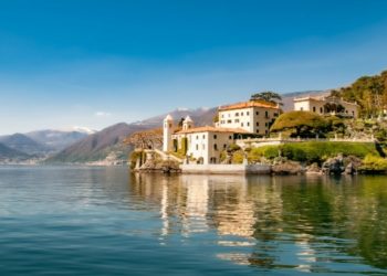 Scenic view of Lake Como featuring a majestic castle surrounded by lush greenery and tranquil waters.