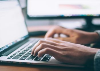 Man typing on a laptop computer, focused on his work in a well-lit environment.