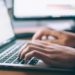 Man typing on a laptop computer, focused on his work in a well-lit environment.