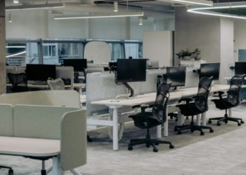 Modern office interior with several desks and ergonomic chairs for employees.