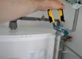 Person holds a wrench, adjusting plumbing, fixing a water heater in a home setting