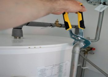 Person holds a wrench, adjusting plumbing, fixing a water heater in a home setting