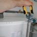 Person holds a wrench, adjusting plumbing, fixing a water heater in a home setting