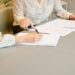 Two women at a table, engaged in signing a contract, with documents laid out in front of them.