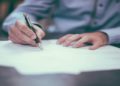 Person signing a document on a piece of paper with a pen.