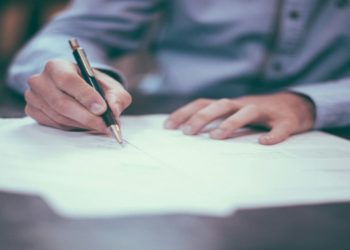 Person signing a document on a piece of paper with a pen.