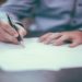 Person signing a document on a piece of paper with a pen.