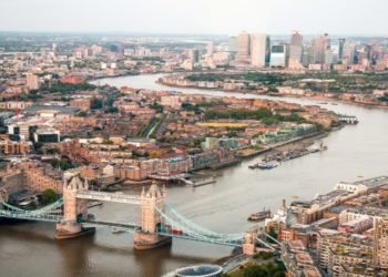 Aerial view of Tower Bridge in London, with the city skyline visible in the background under a clear blue sky.