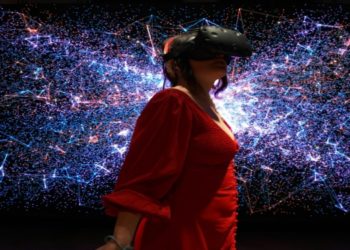 Woman in a red dress wears a VR headset, standing in front of a vibrant digital backdrop with blue and pink glowing lines, creating a futuristic feel.