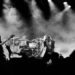 Black and white image of a rock band performing on stage. The lead singer passionately sings at the center, surrounded by dramatic smoke and dynamic lighting.