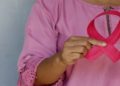 Person in a pink blouse holds a pink ribbon, a symbol of breast cancer awareness