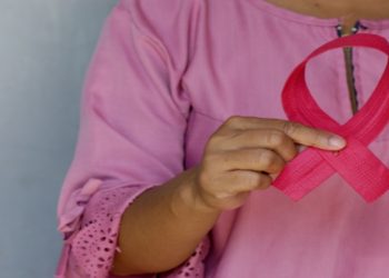 Person in a pink blouse holds a pink ribbon, a symbol of breast cancer awareness