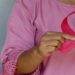 Person in a pink blouse holds a pink ribbon, a symbol of breast cancer awareness