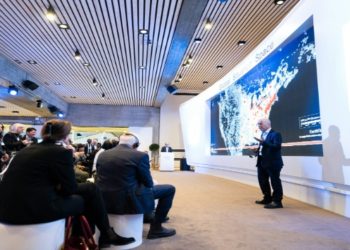 Speaker at the World Economic Forum presents data on a large screen in a modern conference room. Attendees sit attentively, creating an engaged atmosphere.