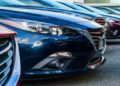Row of parked cars, predominantly blue and red, are closely aligned in a dealership lot. Sleek designs and glossy finishes convey a modern, polished look.