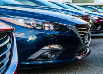 Row of parked cars, predominantly blue and red, are closely aligned in a dealership lot. Sleek designs and glossy finishes convey a modern, polished look.
