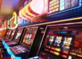 Row of brightly lit slot machines in a casino emits neon lights in red, blue, and orange tones, creating an exciting and lively atmosphere.