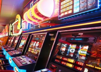 Row of brightly lit slot machines in a casino emits neon lights in red, blue, and orange tones, creating an exciting and lively atmosphere.