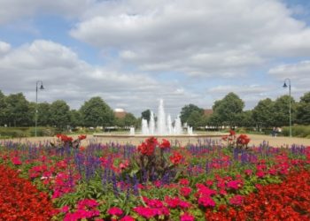 Vibrant flower garden with red and pink blooms, purple accents, and a central fountain in Hertfordshire, England