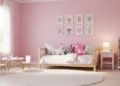 Cozy pink children's room with wall art, a daybed covered in cushions and a pink unicorn plushie. A small round table and chairs sit by a window. A bookshelf and nightstand with a lamp complete the inviting, playful space.