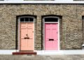 Two vibrant doors on a brick townhouse; left door is peach, numbered 17, and right door is bright pink in London, United Kingdom. The scene is sunny and inviting.