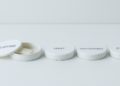 Four white circular tins with labels: Nicotine (lid open showing pouches), Mint, Wintergreen, and Citrus. Minimalist design on a plain surface.