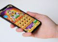 Hand holds a smartphone displaying a colorful slot machine game with an Egyptian theme. The screen shows icons and bright graphics, evoking excitement and fun.
