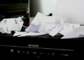Cluttered Epson printer covered with crumpled and folded paper, creating a disorganized and chaotic appearance, suggesting frustration or a busy work environment.