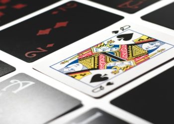 Close-up of playing cards arranged on a white surface. The queen of spades is prominently displayed among red and black cards, conveying a playful tone.