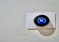 Digital thermostat on a textured white wall displays a temperature of 63 degrees. The sleek, round design conveys modernity and efficiency.