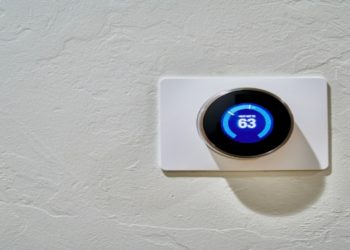 Digital thermostat on a textured white wall displays a temperature of 63 degrees. The sleek, round design conveys modernity and efficiency.