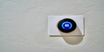 Digital thermostat on a textured white wall displays a temperature of 63 degrees. The sleek, round design conveys modernity and efficiency.