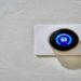 Digital thermostat on a textured white wall displays a temperature of 63 degrees. The sleek, round design conveys modernity and efficiency.
